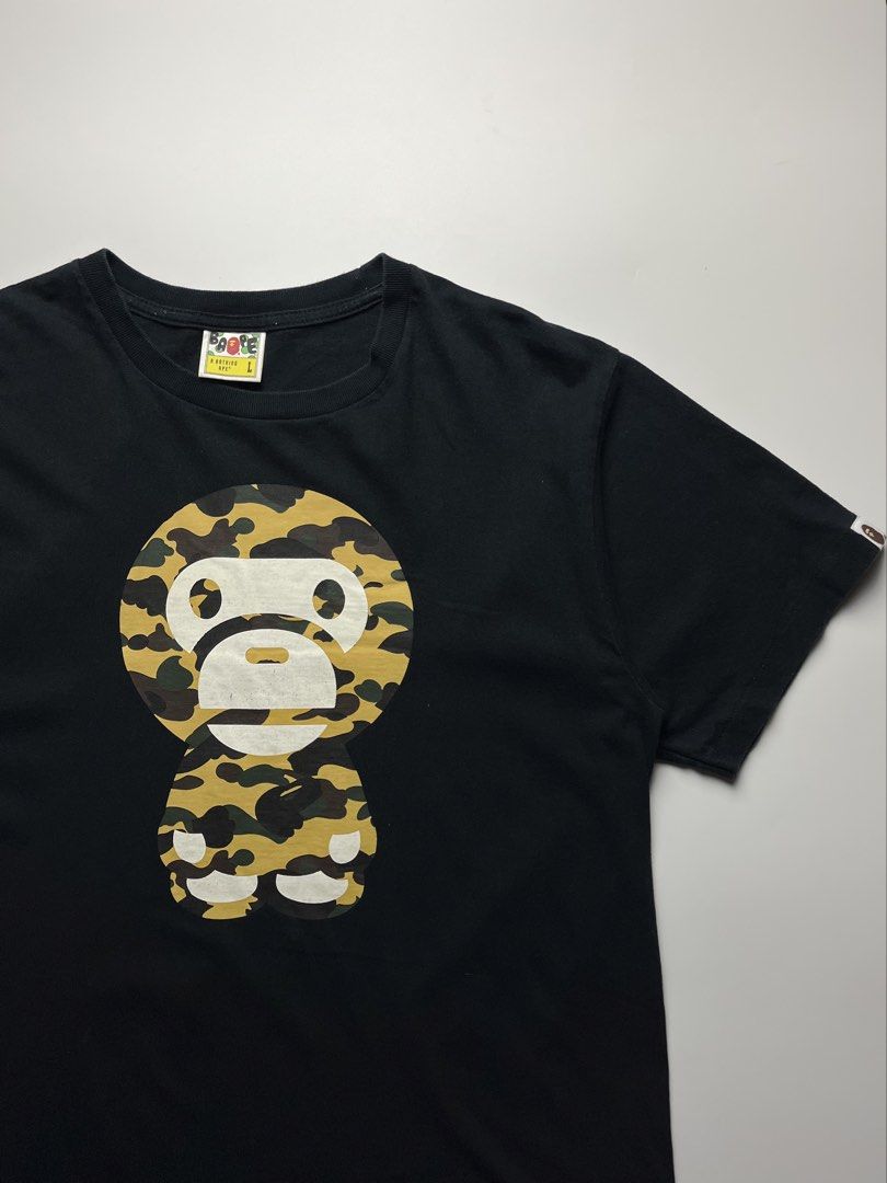 BAPE “Baby Milo” Camouflage Tee (Category: Tshirts & Polo Shirts ) located in Manila. Submitted by streetsavvy (Listing ID 1465863963, Image 2). Description: BAPE “Baby Milo” Camouflage Tee Size: Large Width: 21” Length: 27.5” Shoulder: 18.5” Sleeve Length: 8.5” Hem: 21.5” Measured in Inches Condition: Very good condition with signs of wear Flaw: Hairline cracks Made in China 100% Cotton .