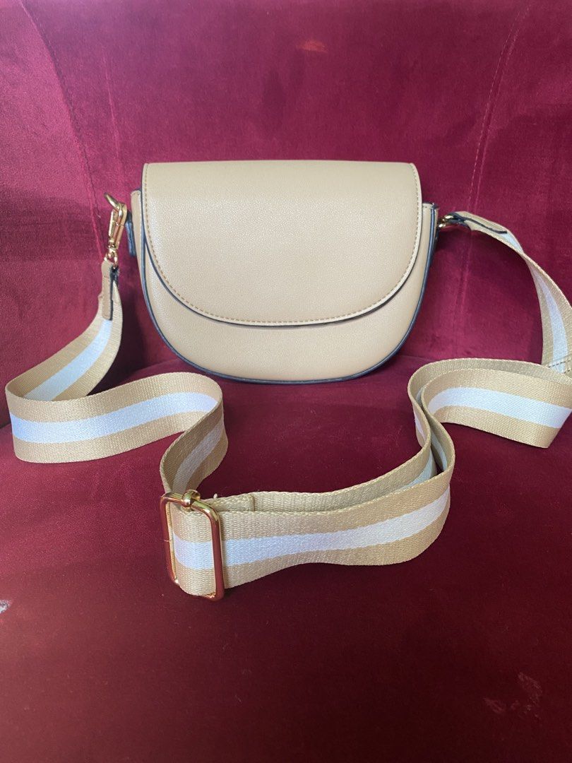 Beige Saddle Crossbody Bag with Striped Strap (Category: Cross-body Bags) located in La Trinidad. Submitted by kinleyky (Listing ID 1465766896, Image 1). Description: - Color: Versatile neutral beige with smooth faux leather finish - Strap: Thick, adjustable white and tan striped pattern - Hardware: Elegant gold-tone accents - Closure: Secure front flap with magnetic snap - Interior: Main compartment, 1 zippered pocket, and 1 open slip pocket - S
