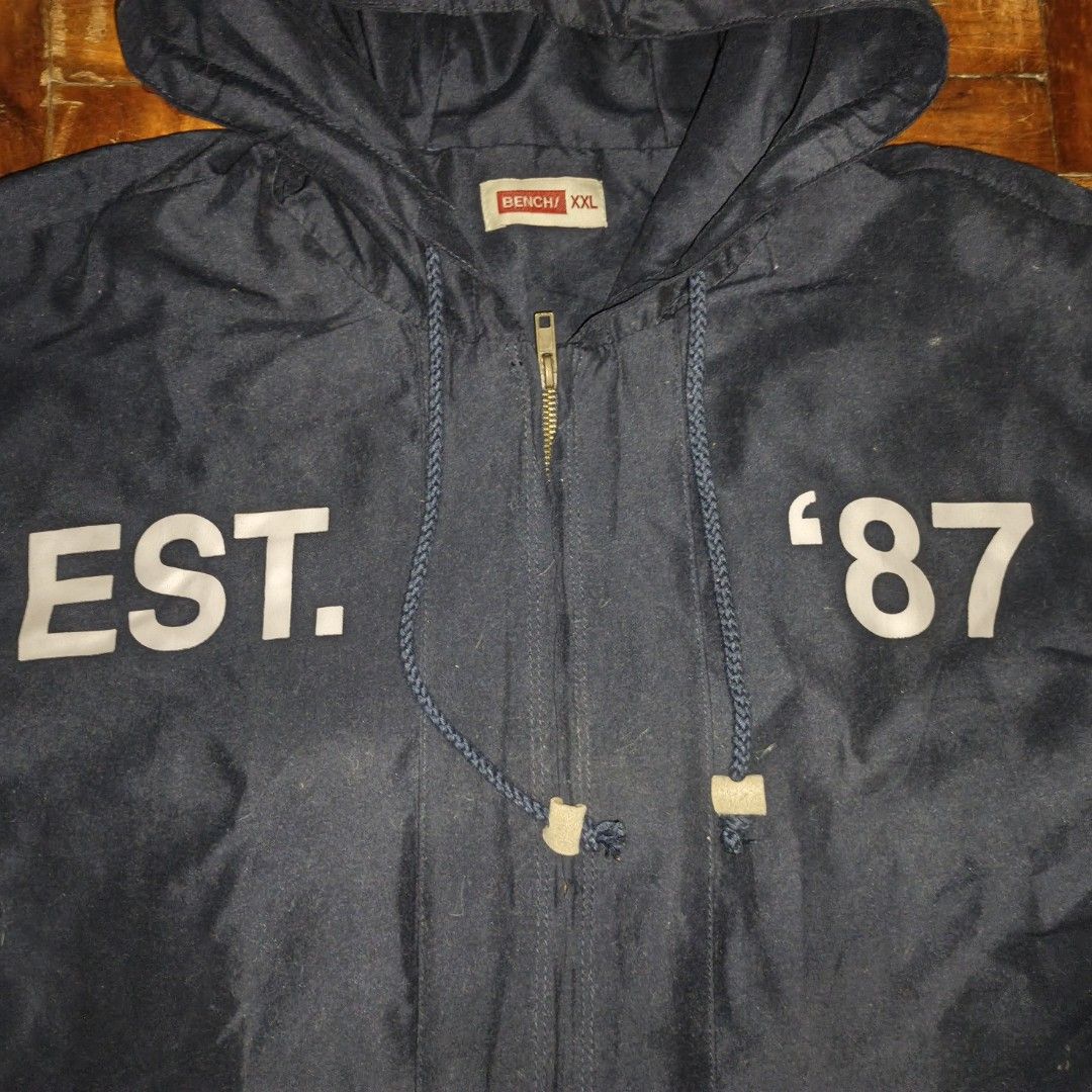 Bench Navy Blue Hooded Jacket Size XXL (Category: Coats, Jackets and Outerwear) located in Manila. Submitted by ekko_0xx (Listing ID 1465885228, Image 3). Description: - Brand: Bench - Color: Dark blue - Size: XXL - Design: Full zip front, adjustable hood and hem drawstrings, large 'EST. 87' white chest lettering - Pockets: Two front pockets with button flaps - Condition/Style: Casual outerwear, great for everyday wear or layering.