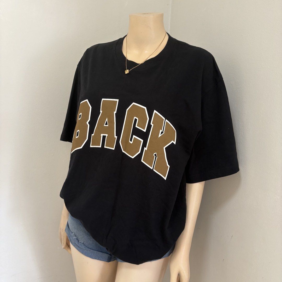 Black Oversized Graphic Shirt (Category: Shirts) located in Imus. Submitted by reloved.nd (Listing ID 1465814227, Image 2). Description: - Style: Casual oversized fit with dropped shoulders - Design: Large brown collegiate 'BACK' letters with white outlines - Neckline: Classic crew neck - Material: Comfortable, breathable cotton - Versatility: Perfect for pairing with denim shorts or jeans - Condition: Brand new / Excellent.