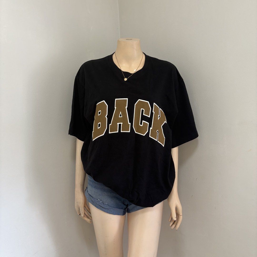 Black Oversized Graphic Shirt (Category: Shirts) located in Imus. Submitted by reloved.nd (Listing ID 1465814227, Image 1). Description: - Style: Casual oversized fit with dropped shoulders - Design: Large brown collegiate 'BACK' letters with white outlines - Neckline: Classic crew neck - Material: Comfortable, breathable cotton - Versatility: Perfect for pairing with denim shorts or jeans - Condition: Brand new / Excellent.