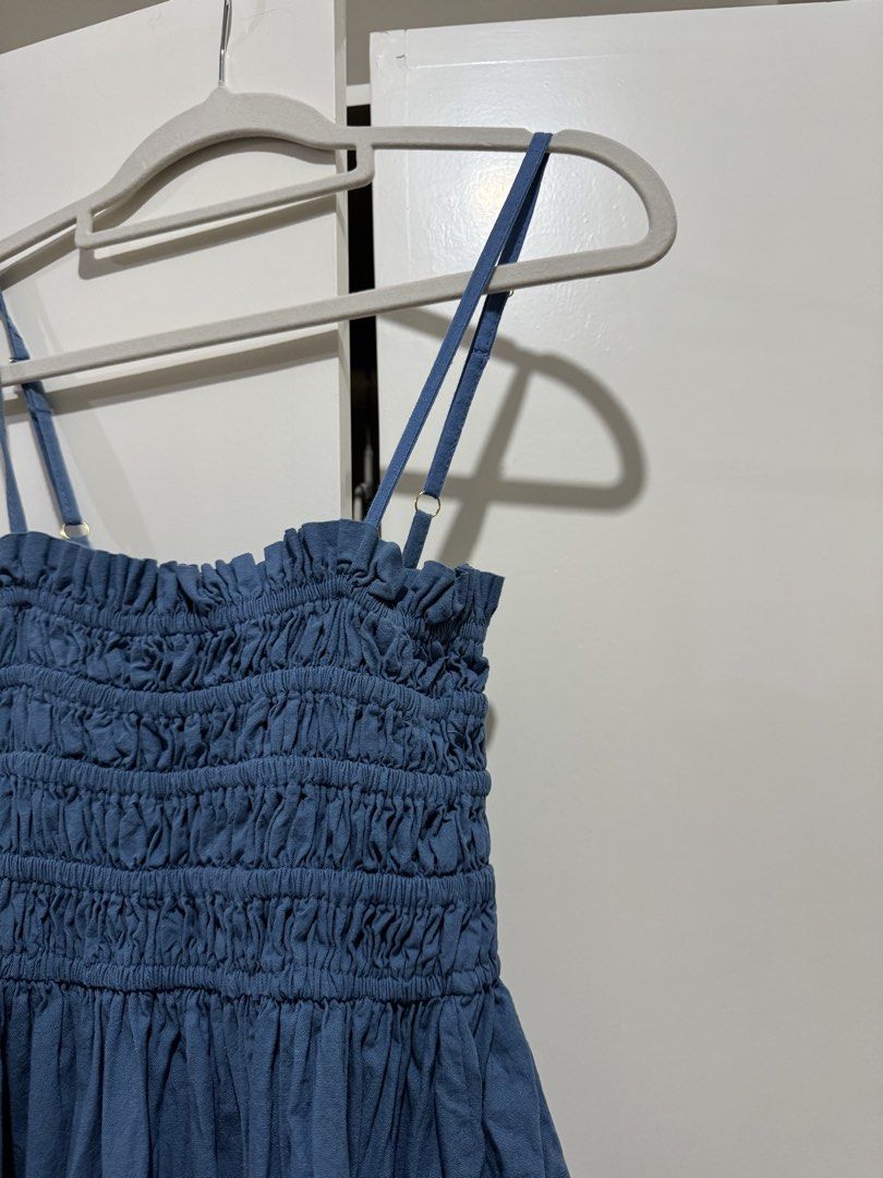 Blue Smocked Midi Dress with Adjustable Straps (Category: Dresses) located in Manila. Submitted by carmela_andd (Listing ID 1465904773, Image 3). Description: - Color: Dusty Blue - Length: Midi - Bodice: Heavily smocked with a ruffled neckline - Straps: Thin, adjustable with gold-tone hardware - Hem: Flowy with a subtle bubble bottom tier - Fabric: Lightweight and breathable - Style: Easy pull-on, perfect for casual days and warm weather.