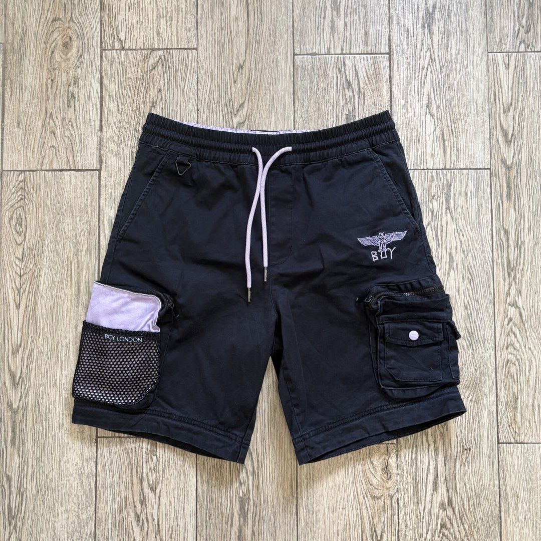 Boy London Cargo Shorts (Category: Shorts) located in Imus. Submitted by reloved.nd (Listing ID 1465812113, Image 1). Description: - Brand: Boy London - Color: Black with light purple drawstring and waist lining - Fit: Relaxed fit with an elastic waistband - Pockets: Multiple utility cargo pockets, including a branded mesh pouch and a zipped pocket - Details: Embroidered Boy London eagle logo on the left leg - Perfect for: Streetwear, casual wear