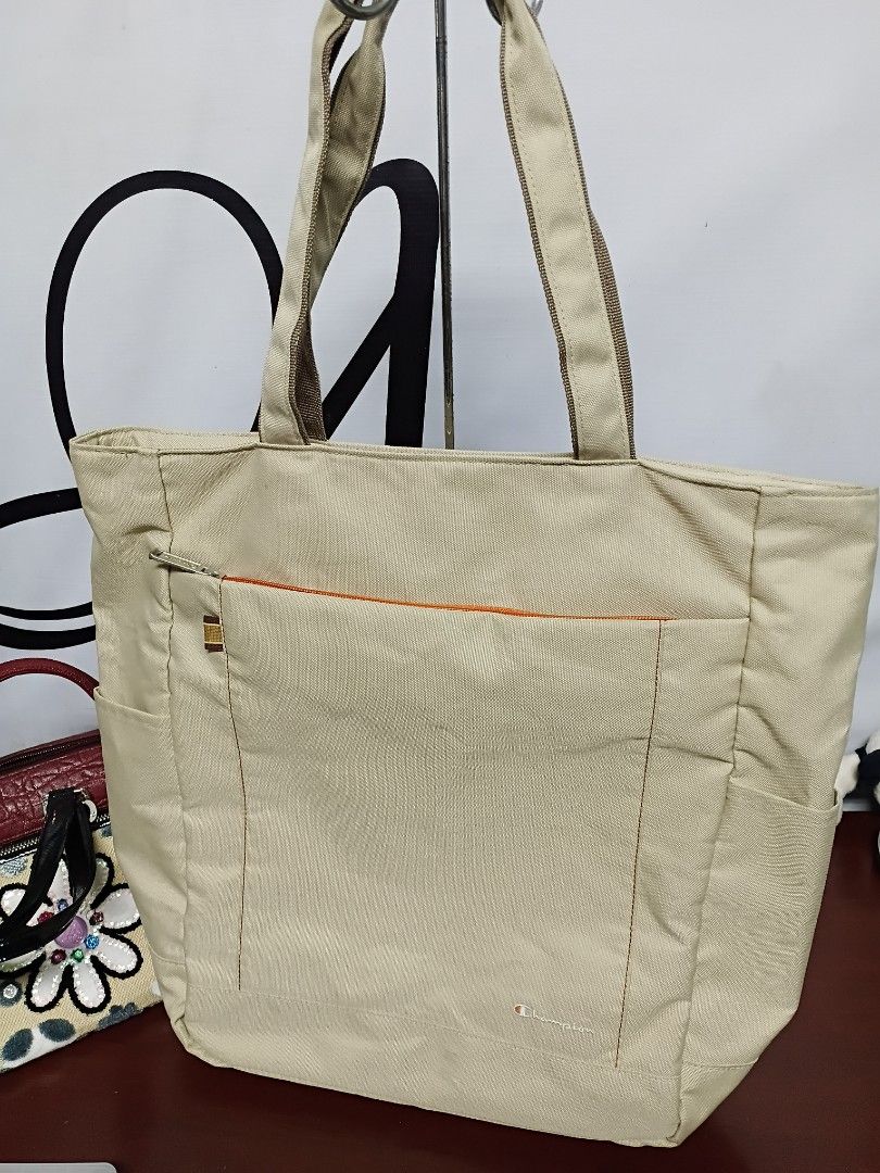 Champion Canvas Tote Bag Beige (Category: Tote Bags) located in Quezon City. Submitted by fateonlineshop (Listing ID 1465797267, Image 1). Description: - Brand: Champion - Color: Beige canvas with a vibrant orange nylon interior - Straps: Sturdy dual shoulder straps for comfortable carrying - Pockets: Large exterior front zip pocket and interior slip pockets for organization - Condition: Clean inside and out, very durable construction - Ideal Use