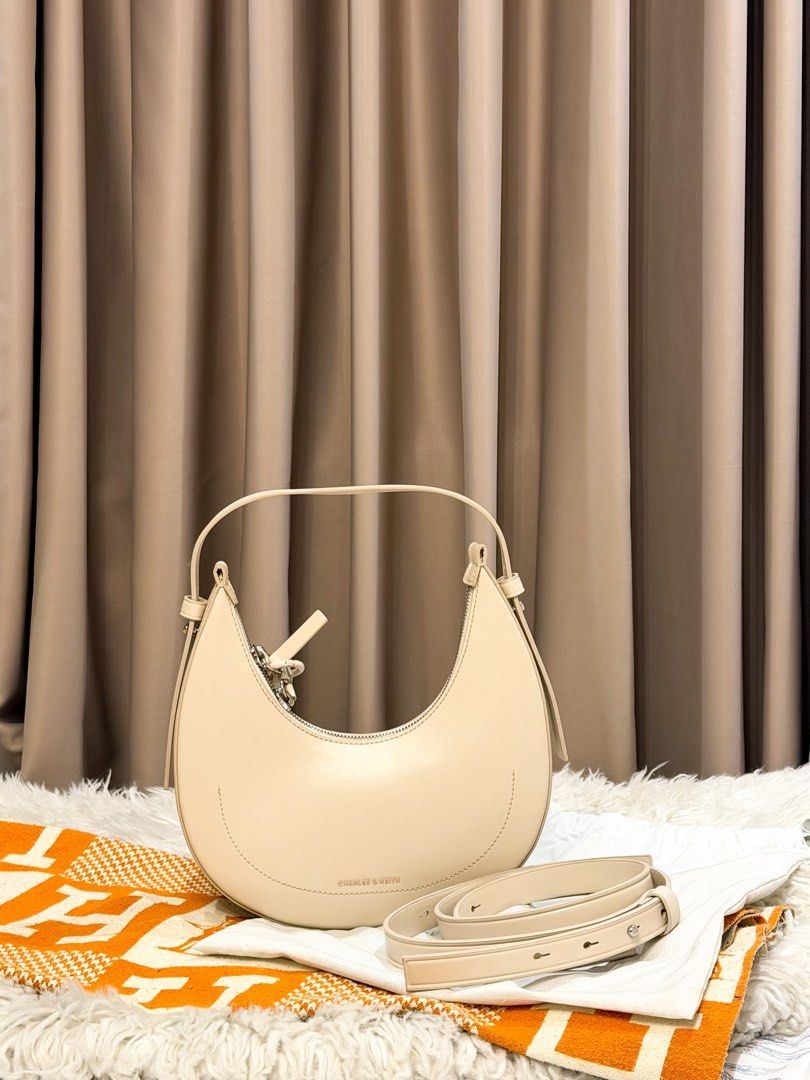 Charles & Keith Cream Crescent Shoulder Bag (Category: Shoulder Bags) located in Manila. Submitted by jairahncle (Listing ID 1465913327, Image 2). Description: - Brand: Charles & Keith - Style: Curved crescent shape bag - Color: Cream with chic silver hardware - Condition: Brand new with tags, includes original dust bag - Features: Clean smooth finish, structured base to hold its shape, and an adjustable extra-long strap inside - RFS: Declutterin