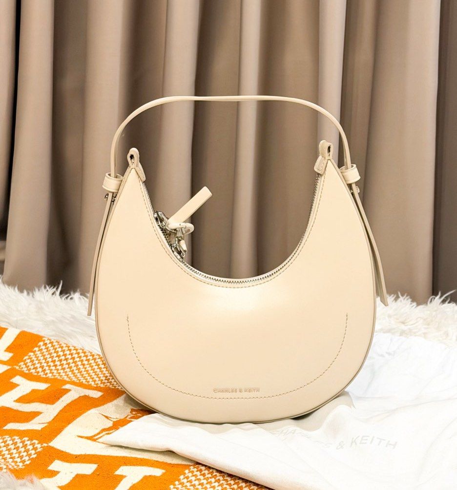 Charles & Keith Cream Crescent Shoulder Bag (Category: Shoulder Bags) located in Manila. Submitted by jairahncle (Listing ID 1465913327, Image 1). Description: - Brand: Charles & Keith - Style: Curved crescent shape bag - Color: Cream with chic silver hardware - Condition: Brand new with tags, includes original dust bag - Features: Clean smooth finish, structured base to hold its shape, and an adjustable extra-long strap inside - RFS: Declutterin