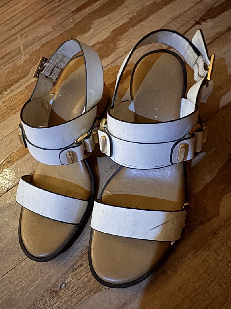 Charles & Keith White Block Heel Sandals Size 35 (Category: Heels) located in Pasig City. Submitted by klaaaaa (Listing ID 1465878155, Image 1). Description: - Brand: Charles & Keith - Style: White sandals with gold block heels, double front straps, and gold buckle hardware - Fit: Slingback strap with adjustable closure, Size 35 - Details: Tan inner sole with clear branding - Condition: Visible wear, creasing on the white material, and some scuff
