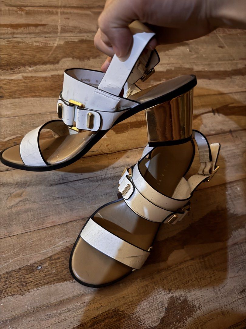 Charles & Keith White Block Heel Sandals Size 35 (Category: Heels) located in Pasig City. Submitted by klaaaaa (Listing ID 1465878155, Image 2). Description: - Brand: Charles & Keith - Style: White sandals with gold block heels, double front straps, and gold buckle hardware - Fit: Slingback strap with adjustable closure, Size 35 - Details: Tan inner sole with clear branding - Condition: Visible wear, creasing on the white material, and some scuff