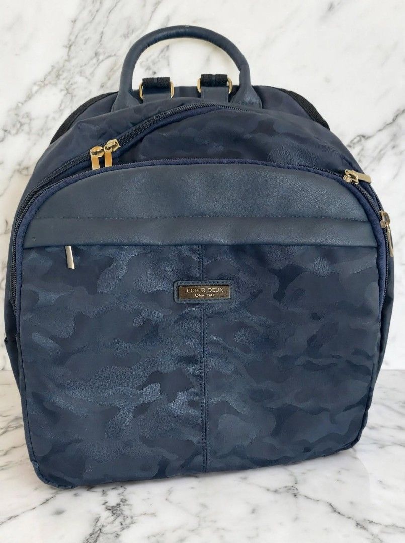 Coeur Deux Moda Italy Blue Camo Backpack (Category: Backpacks) located in Caloocan City. Submitted by chonadura91470 (Listing ID 1465777029, Image 1). Description: - Brand: Coeur Deux Moda Italy - Design: Navy blue camouflage pattern with metal hardware and front branded badge - Storage: Zippered main compartment and front pocket - Comfort: Adjustable shoulder straps and convenient top grab handle - Interior: Brown silky fabric lining - Condition