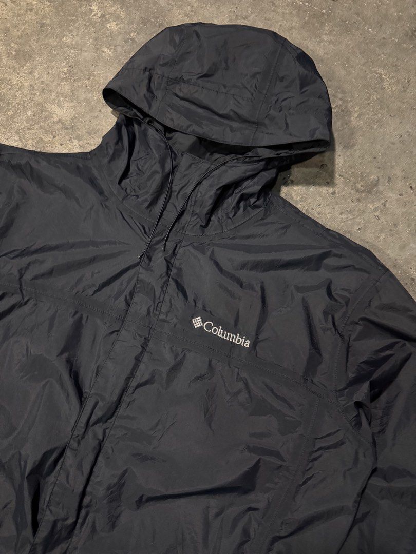 Columbia Black Hooded Windbreaker Jacket (Category: Coats, Jackets and Outerwear) located in Pasig City. Submitted by dripthrift1600 (Listing ID 1465950037, Image 3). Description: - Brand: Columbia - Color: Classic Black - Size: Check measurements (DM for exact fit) - Material: Lightweight, packable nylon with breathable mesh lining - Features: Attached hood, full zip closure with Velcro storm flap, adjustable drawstrings at hood and bottom hem -