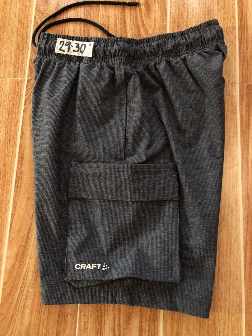 Craft Dark Grey Cargo Shorts (Category: Shorts) located in Tarlac. Submitted by f8njcgvfqy90581 (Listing ID 1465898467, Image 3). Description: - Brand: Craft - Color: Dark grey with textured fabric - Size: 29-30 (tagged on waist) - Waistband: Elastic with adjustable black drawstring - Pockets: Large cargo pocket on the right leg - Branding: Distinct white Craft logo on the cargo pocket.