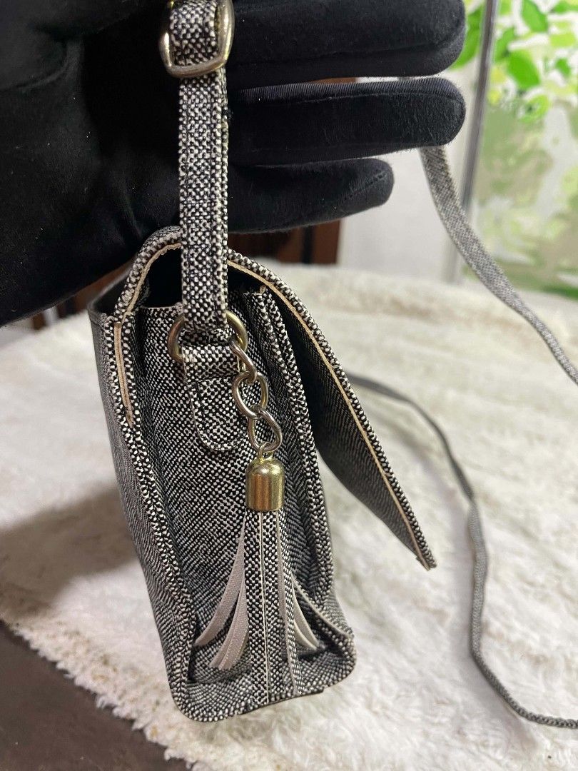 Crossbody Bag with Tassel (Category: Cross-body Bags) located in Naawan. Submitted by twilly.apparel2 (Listing ID 1465845300, Image 2). Description: - Material/Design: Black and white textured tweed with a metal bar accent on the flap top - Accessories: Includes a removable beige tassel charm - Strap: Long, adjustable shoulder strap for comfortable wear - Size: Measures approximately 8 inches across - Condition: Good overall condition with a mino