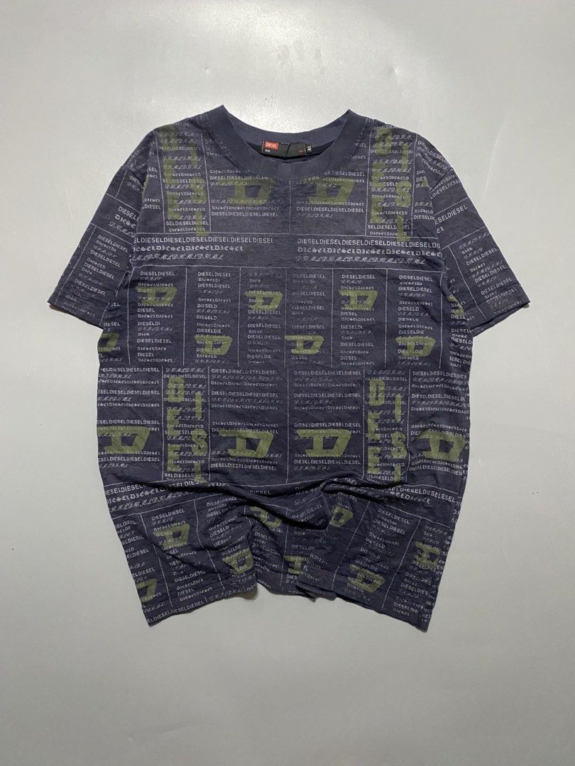 Diesel All Over Print Logo Tee Size XL (Category: Tshirts & Polo Shirts ) located in Manila. Submitted by delunakenn94368 (Listing ID 1465904320, Image 1). Description: - Brand: Diesel - Color: Dark navy blue with muted olive green accents - Size: XL (Regular fit) - Design: All-over grid and text pattern with repeating brand name and 'D' logos - Features: Short sleeves, crew neckline, black woven neck tag with red Diesel box logo - Material: Soft