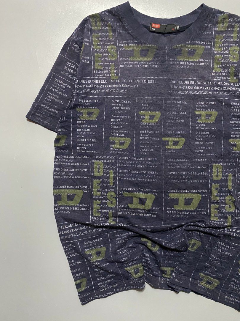 Diesel All Over Print Logo Tee Size XL (Category: Tshirts & Polo Shirts ) located in Manila. Submitted by delunakenn94368 (Listing ID 1465904320, Image 2). Description: - Brand: Diesel - Color: Dark navy blue with muted olive green accents - Size: XL (Regular fit) - Design: All-over grid and text pattern with repeating brand name and 'D' logos - Features: Short sleeves, crew neckline, black woven neck tag with red Diesel box logo - Material: Soft