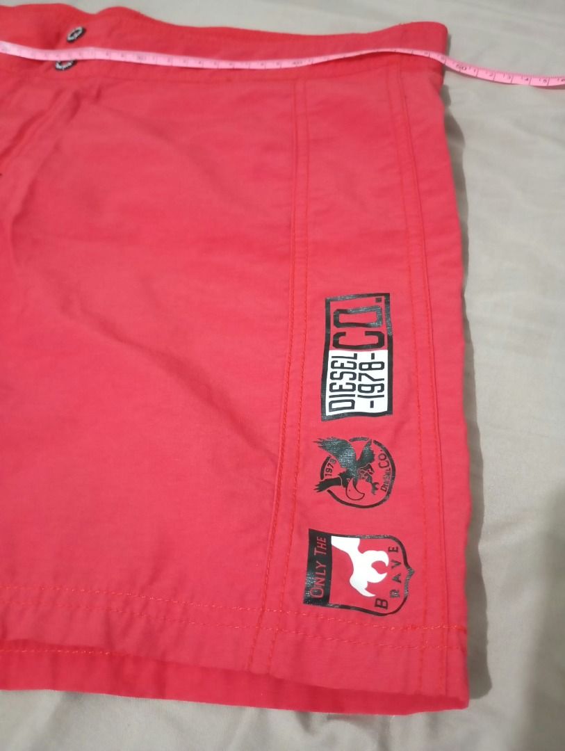 Diesel Red Swim Shorts (Men) (Category: Shorts) located in Pasig City. Submitted by ajms63804 (Listing ID 1465783180, Image 2). Description: - Brand: Diesel - Size: Fits 36" to 38'" - Color: Red with black side panels - Details: Graphic logo print on lower left leg - Pocket: Single back pocket with button closure - Fit: Comfortable for beach days or casual wear - Sizing: Waistband measurement shown in photos.