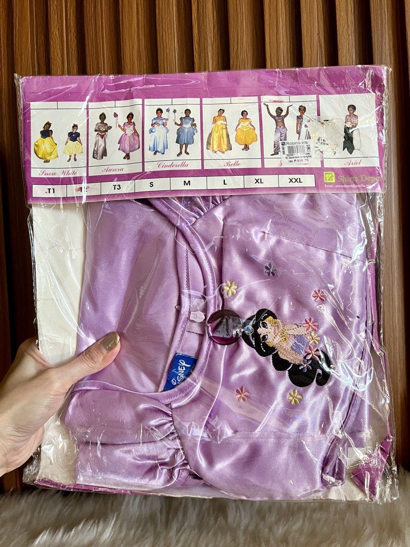 Disney Princess Jasmine Costume Set (Category: Babies & Kids Fashion) located in Navotas City. Submitted by mommybabyc (Listing ID 1465877868, Image 2). Description: - Brand new and unopened Disney Princess Jasmine costume - Still sealed in original plastic packaging with header card - Purple satin top featuring sheer mesh sleeves - Detailed with an embroidered Jasmine graphic and a large decorative gemstone at the neckline - Header card displays