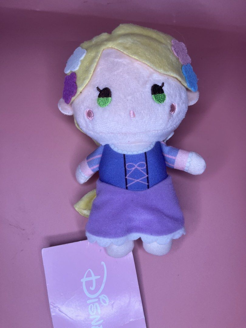 Disney Rapunzel SEGA Plush Toy (Category: Plushies & Soft Toys) located in Caloocan City. Submitted by snapshop_ph (Listing ID 1465801633, Image 1). Description: Rapunzel plush from Sega with Disney hologram tag. Blonde hair styled in a braid with felt flower hair clips. Purple dress with pink ribbon details on the bodice and a white ruffled hem. Stands about handheld size. Original tag attached at the bottom..