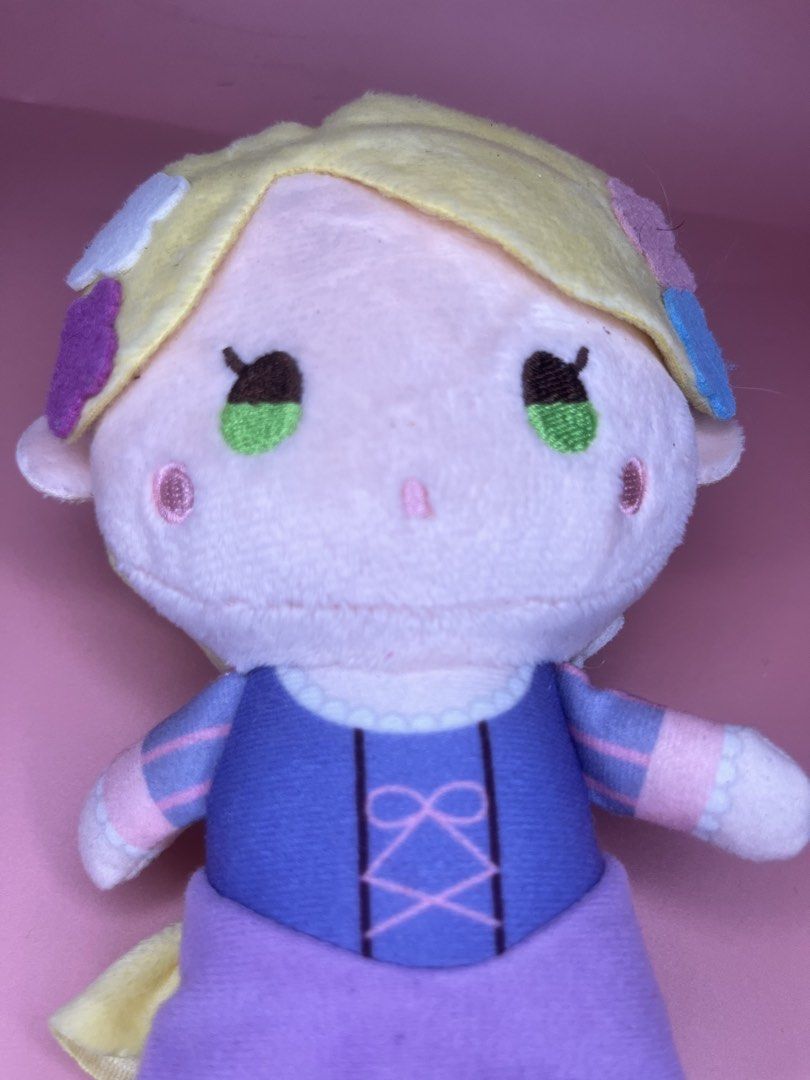 Disney Rapunzel SEGA Plush Toy (Category: Plushies & Soft Toys) located in Caloocan City. Submitted by snapshop_ph (Listing ID 1465801633, Image 2). Description: Rapunzel plush from Sega with Disney hologram tag. Blonde hair styled in a braid with felt flower hair clips. Purple dress with pink ribbon details on the bodice and a white ruffled hem. Stands about handheld size. Original tag attached at the bottom..