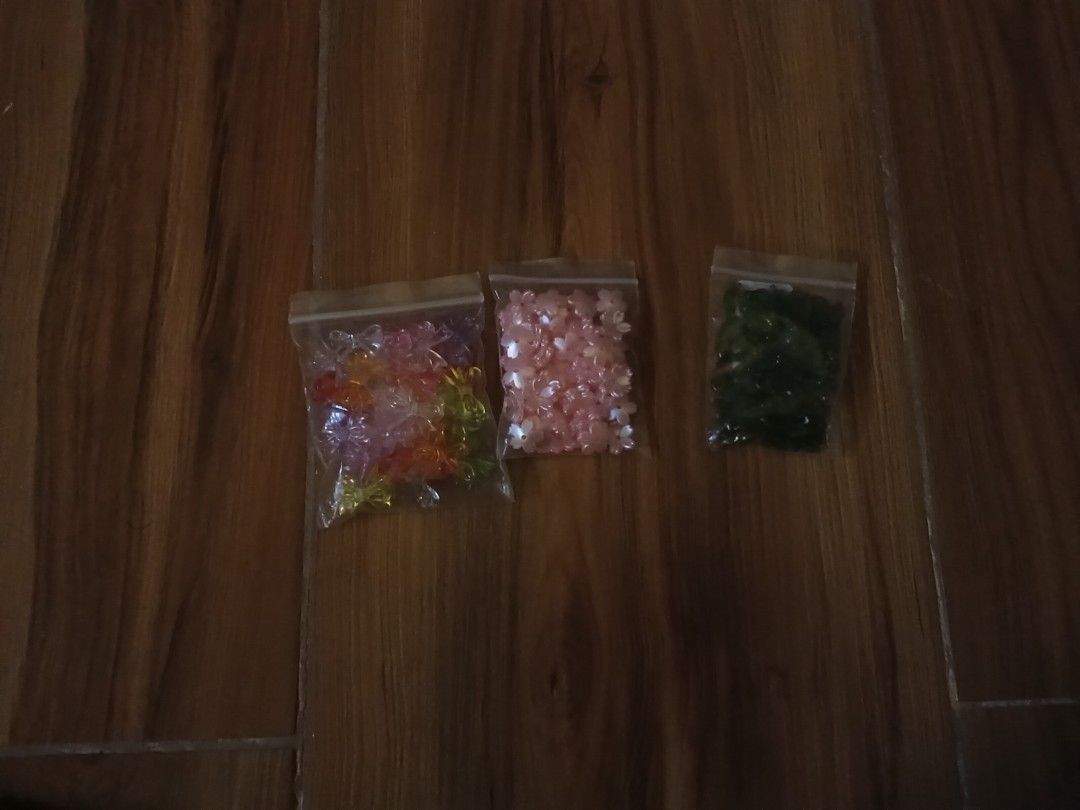 DIY flower shape craft beads in three bags (Category: Craft Supplies & Tools) located in Manila. Submitted by fleurinie.ph (Listing ID 1465838676, Image 1). Description: - 3 bags of small flower-shaped beads for jewelry making and crafts - Left bag: Mixed transparent colors (pink, orange, yellow, purple) - Middle bag: Solid pink cherry blossom beads - Right bag: Dark green beads - Conveniently packed in clear ziplock bags - Great stash for handma