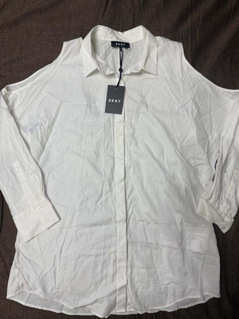 DKNY White Cold Shoulder Button-Up Shirt (Category: Shirts) located in Quezon City. Submitted by mt031199 (Listing ID 1465947437, Image 1). Description: - Brand: DKNY (Original tag still attached) - Color: Classic White - Style: Button-up shirt with trendy cold shoulder cutouts on both sleeves - Features: Long sleeves with button cuffs, classic collar, and front button placket - Condition: Brand new with tags (BNWT).