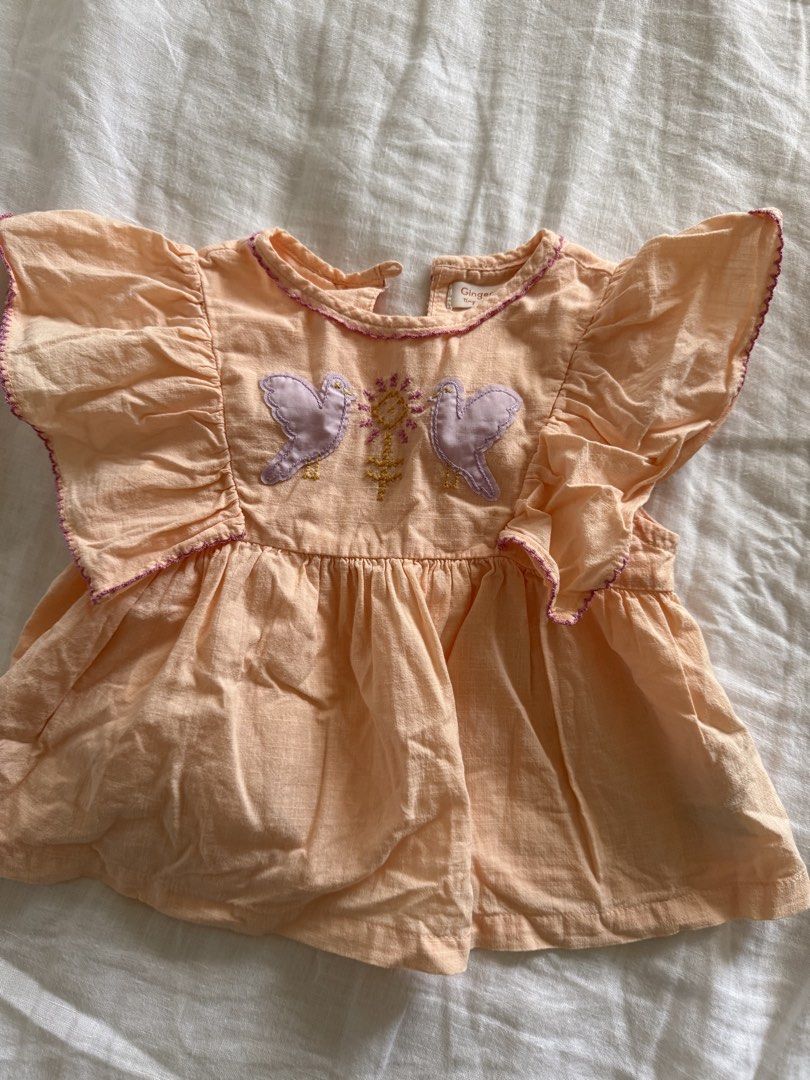 Gingersnaps Tiny Peach Bird Embroidered Flutter Sleeve Top 2Y (Category: Babies & Kids Fashion) located in Taguig. Submitted by muntingkahon (Listing ID 1465765813, Image 1). Description: - Brand: Gingersnaps Tiny - Size: 2Y (fits heights 87-92 cm) - Color: Peach with purple contrast stitching on flutter sleeves and collar - Design: Sweet embroidered purple birds and floral details on the front - Closure: Convenient button closure at the back nec