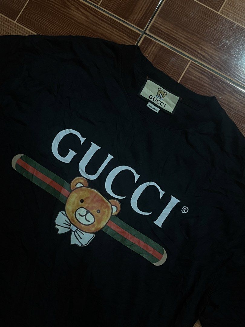 Gucci Black Bear Graphic T-Shirt (Category: Tshirts & Polo Shirts ) located in Manila. Submitted by cycy16_2004 (Listing ID 1465765908, Image 2). Description: - Brand: Gucci - Color: Black - Material: 100% Cotton - Design: Large playful bear graphic over signature green and red stripe on front, pink circular logo patch on back - Details: Short sleeves, round neckline, Made in Italy label, and interior care tags attached - Condition: Excellent cas