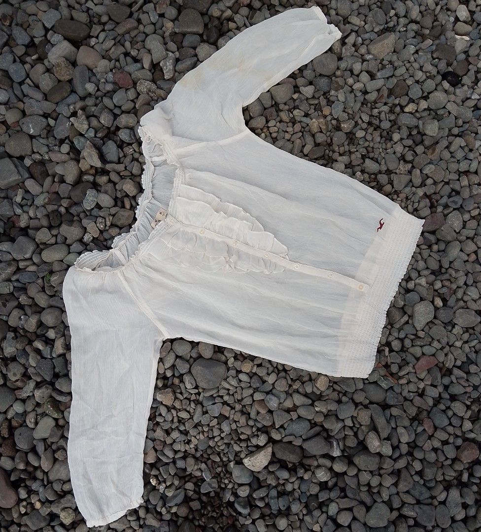 Hollister Off Shoulder Ruffle Blouse White Medium (Category: Blouses) located in Kapalong. Submitted by aliclothesfinds21 (Listing ID 1465823465, Image 3). Description: - Brand: Hollister - Color: White - Size: Medium - Fabric: Sheer, lightweight, and breezy - Design: Button-down front, ruffled center panel, smocked collar and hem - Details: Long sleeves with ruffled elastic cuffs, subtle embroidered seagull logo near the hem - Style: Classic boh