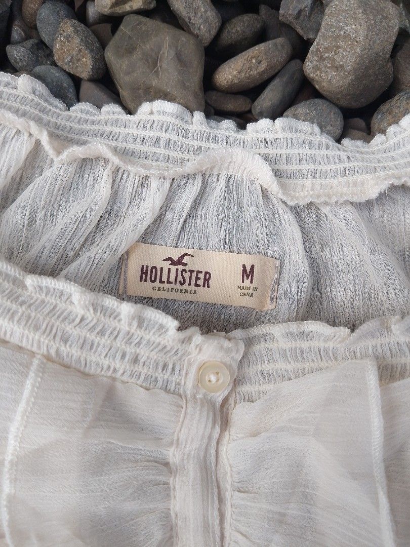 Hollister Off Shoulder Ruffle Blouse White Medium (Category: Blouses) located in Kapalong. Submitted by aliclothesfinds21 (Listing ID 1465823465, Image 1). Description: - Brand: Hollister - Color: White - Size: Medium - Fabric: Sheer, lightweight, and breezy - Design: Button-down front, ruffled center panel, smocked collar and hem - Details: Long sleeves with ruffled elastic cuffs, subtle embroidered seagull logo near the hem - Style: Classic boh