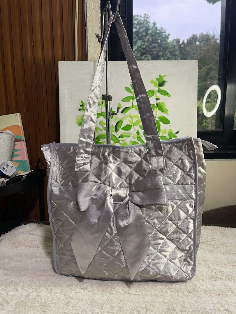 Inter Pack Quilted Silver Tote Bag with Bow (Category: Tote Bags) located in Naawan. Submitted by twilly.apparel2 (Listing ID 1465851477, Image 1). Description: - Brand: Inter Pack (Made in Thailand) - Material: Shimmery silver quilted satin - Design: Stylish big matching bow on the front with double shoulder straps - Closure: Secure zipper top - Dimensions: Approx. 14" across x 13" down - Best For: Daily use, school, or quick errands - Condition