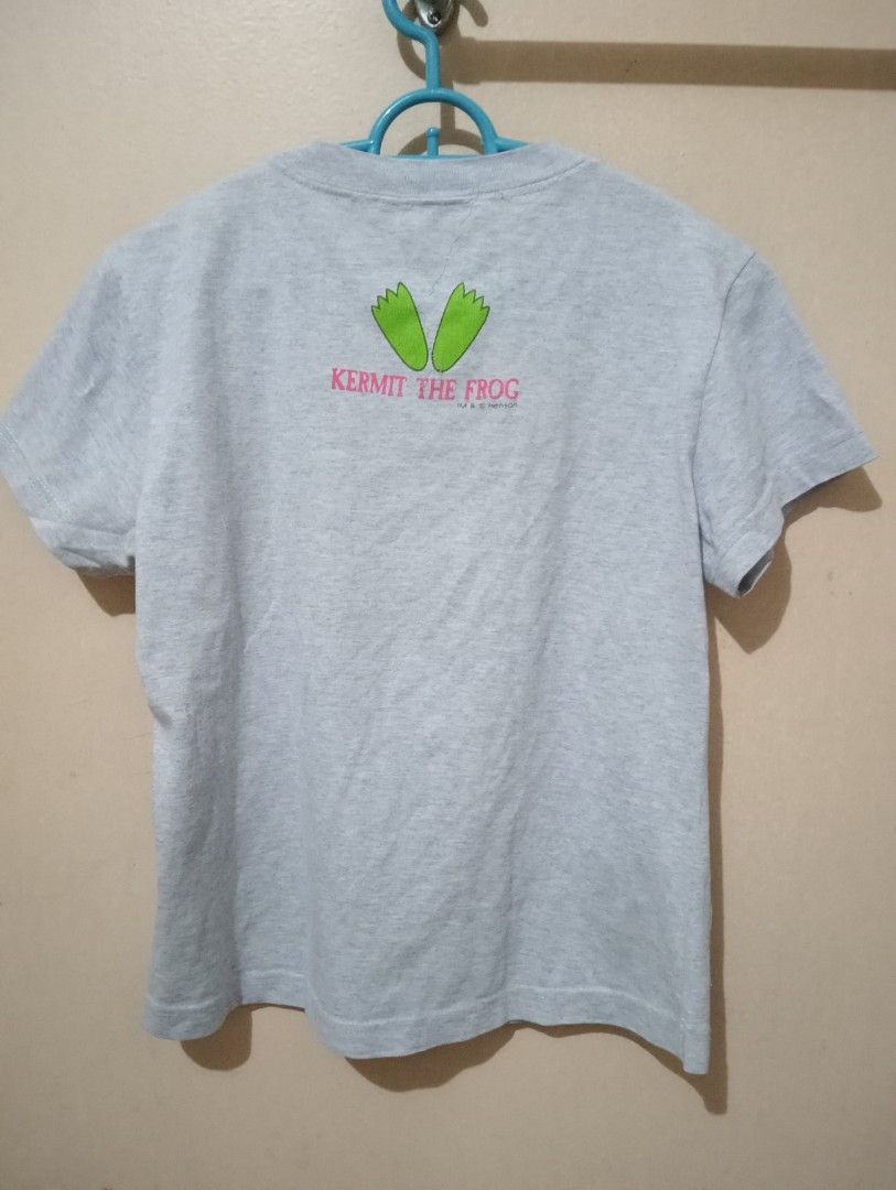 Kermit The Frog Grey T-Shirt (Category: Shirts) located in Makati City. Submitted by YSL80022 (Listing ID 1465896508, Image 2). Description: - Authentic Kermit Collection graphic tee in grey from Gift Gate in the early 2000's - Tag size: 14 - Design: 3 front panels showing Kermit in various poses with pink lettering - Detail: Small green frog feet logo printed near the back collar - Fit & Style: Short sleeves and classic crew neckline - Material: