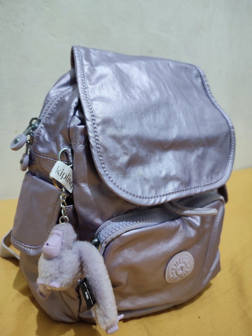 Kipling Metallic Purple Mini Backpack with Monkey Keychain (Category: Backpacks) located in Bacoor. Submitted by almfl (Listing ID 1465900585, Image 2). Description: - Brand: Kipling - Style: Mini Backpack - Color: Shiny Metallic Purple with light purple interior lining - Closure: Main flap with drawstring - Pockets: Zippered front pocket, interior zipper compartment, and open slip pocket - Extras: Includes signature Bibi fuzzy monkey keychain an