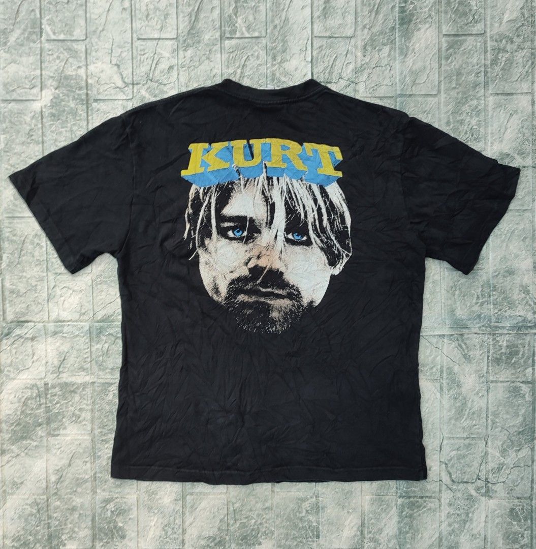 Kurt Cobain Nirvana Graphic Black T-Shirt (Category: Tshirts & Polo Shirts ) located in Bayambang. Submitted by mon10192816 (Listing ID 1465879452, Image 2). Description: - Width 22 - Length 27.5 - Brand/Tag: Ice Valley - Size: Large - Color: Black - Material: Soft cotton, regular fit - Design: Kurt Cobain guitar graphic with yellow splatter on the front; large close-up portrait with blue eyes and name on the back - Style: Short sleeves, grunge/r