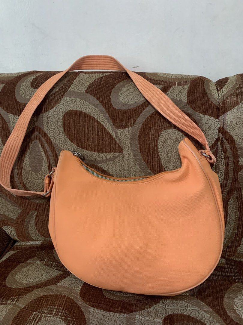 Lacoste Peach Crossbody Shoulder Bag (Category: Cross-body Bags) located in Las Pinas. Submitted by vanethneth (Listing ID 1465882611, Image 2). Description: - Peach Lacoste crossbody bag with a trendy curved crescent shape - Adjustable strap for a comfortable, customized fit - Convenient front zipped pocket and secure main zip closure - Stylish green and white striped fabric lining with an internal zip pocket - Accented with classic silver-toned