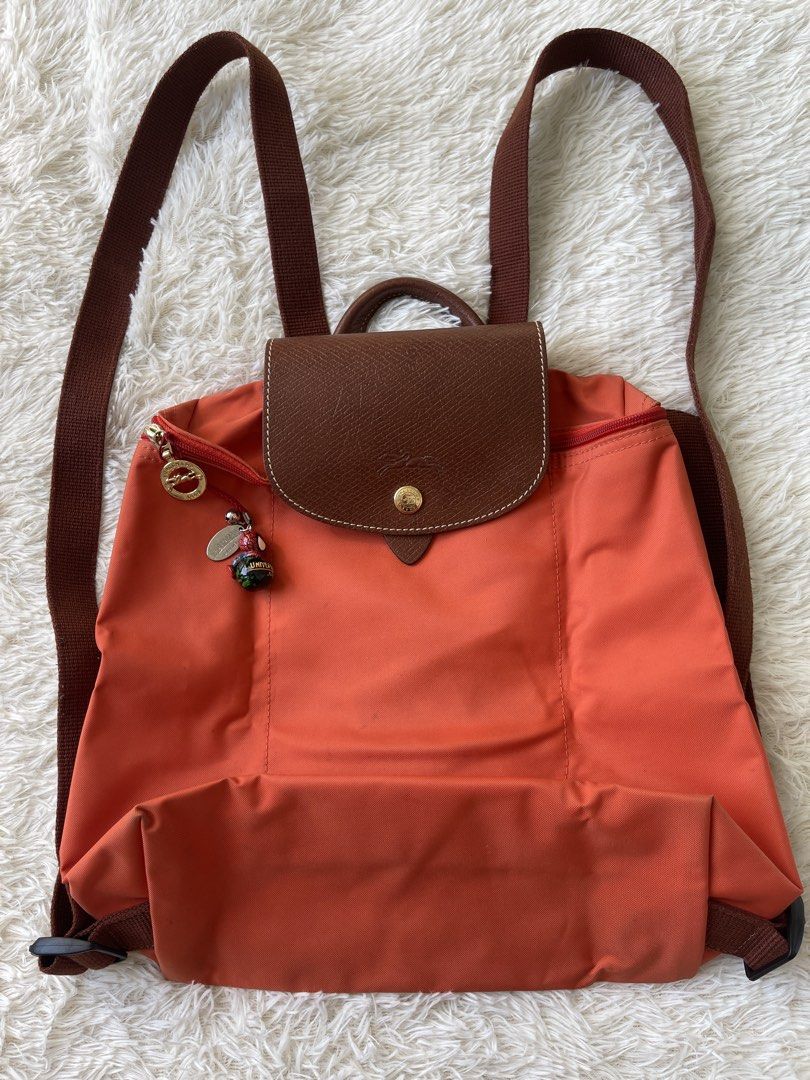 Longchamp Le Pliage Orange Nylon Backpack (Category: Backpacks) located in Malolos. Submitted by ishnnt (Listing ID 1465907929, Image 2). Description: - Brand: Longchamp - Color: Vibrant Orange with Brown Leather flap and straps - Material: Durable, easy-to-clean nylon with gold-tone hardware - Design: Lightweight, foldable, and packs completely flat - Inclusion: Comes with an adorable Spider-Man zipper charm - Flaws: Minor dirt marks/stains near