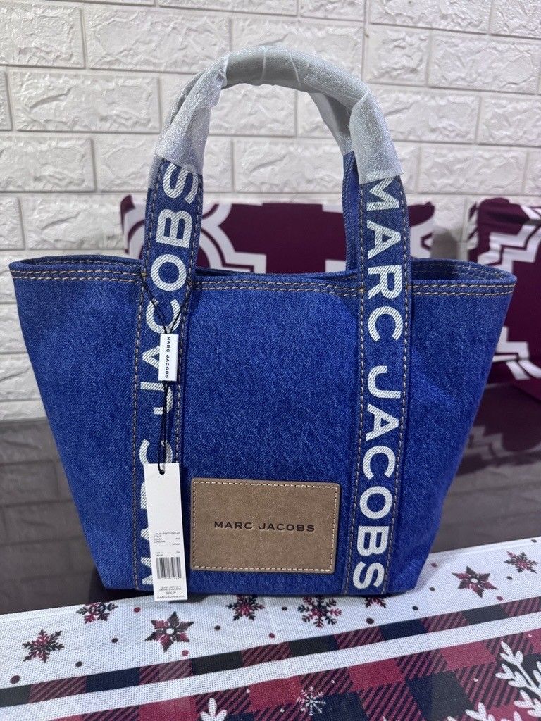 Marc Jacobs Denim Tote Bag (Category: Tote Bags) located in Manila. Submitted by keirye (Listing ID 1465773563, Image 2). Description: - Brand: Marc Jacobs - Material: Blue denim with brown leather details - Condition: Brand new with tags and handle wrapping - Design: Bold white logo lettering and front embossed leather patch - Features: Spacious open-top design, perfect for daily essentials - Guaranteed authentic - Mode of Payment: BPI, GCash/ o