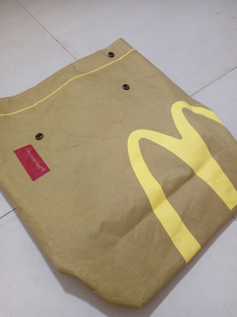 McDonald's Brown Canvas Tote Backpack (Category: Backpacks) located in Manila. Submitted by adrianloqu02215 (Listing ID 1465903065, Image 1). Description: - Brand: McDonald's - Material: Durable heavy-duty canvas fabric in a neutral brown earth-tone - Design: Large yellow golden arches logo on the front with a red 'i'm lovin' it' tag - Closure: Secure snap button closure on the upper section - Straps: Comfortable, adjustable back straps.