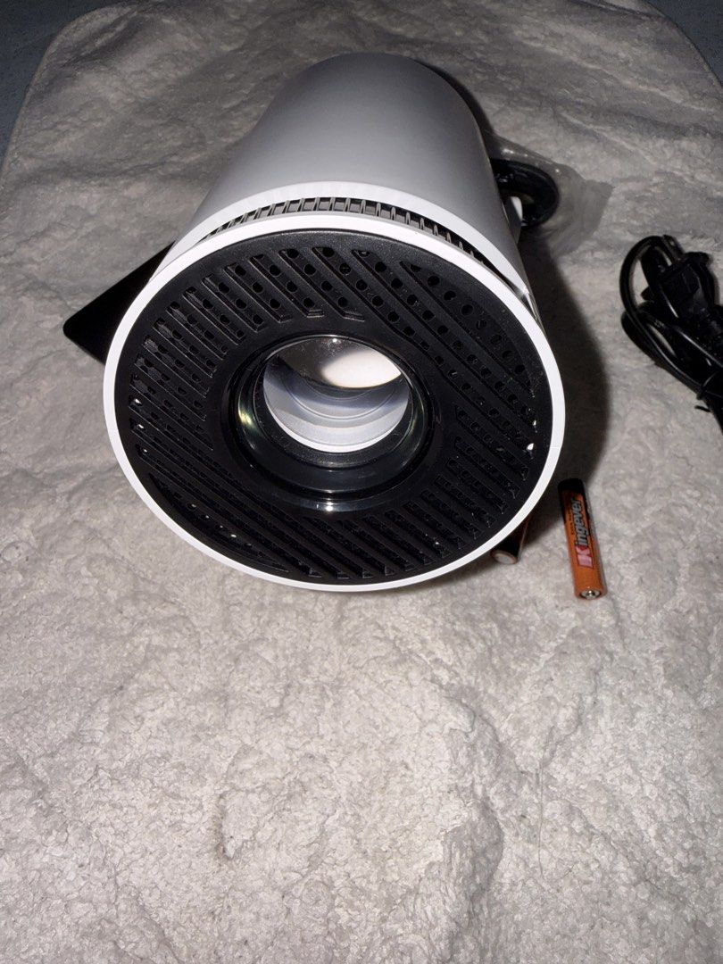 Mini portable projector with power cable and batteries (Category: Projectors) located in Manila. Submitted by gwessyj1829939 (Listing ID 1465789356, Image 1). Description: - Cylindrical white mini projector with a stylish black circular front grille - Compact and portable size, perfect for desks or tables - Includes power cord and two AAA batteries so you can use it right away - Features an adjustable stand for easy angle customization - Ideal fo