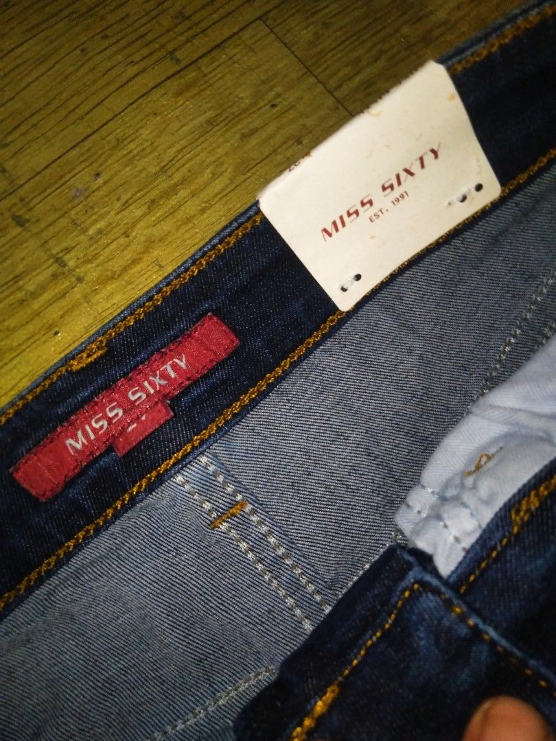 Miss Sixty Flare Dark Wash Jeans (Category: Jeans) located in Manila. Submitted by jaradhiggins24 (Listing ID 1465866813, Image 3). Description: - Brand: Miss Sixty (Est. 1991) - Style: Dark wash denim flare jeans with high-rise waist - Details: Contrast yellow stitching, distressed coin pocket with red logo tag, and leather back patch - Closure: Button closure and zipper fly - Condition: Brand new with original tags attached.