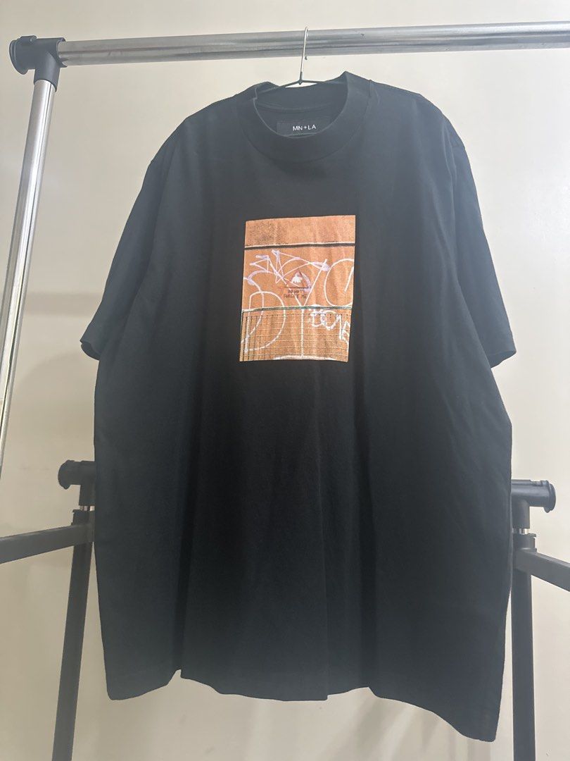 MN+LA Black Graphic T-Shirt (Category: Tshirts & Polo Shirts ) located in Manila. Submitted by royal_vintage_thriftshop (Listing ID 1465810947, Image 1). Description: Black t-shirt from MN+LA. Heavyweight cotton fabric with a structured ribbed collar. Graphic print on the chest featuring a fence and abstract graffiti art with text detail. Size large, relaxed fit. Width measures 25 inches, length is 29 inches based on the official size chart. Mini