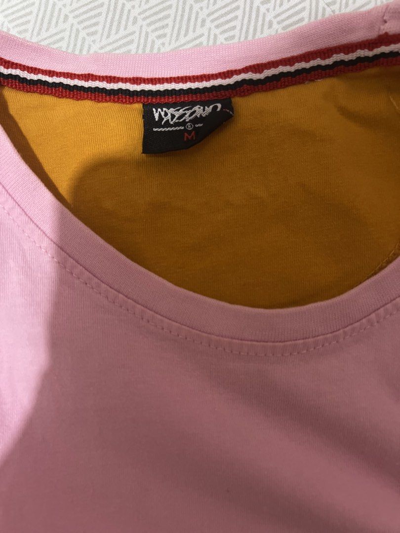 Mossimo Pink T-Shirt Size M (Category: Shirts) located in Manila. Submitted by kaceylgt (Listing ID 1465924506, Image 3). Description: - Brand: Mossimo - Color: Pink with yellow and mustard yellow accents - Size: M - Design: Yellow embroidered chest branding - Details: Layered mustard yellow inner collar with striped trim, plus a small fabric patch near the bottom hem - Condition: Excellent.