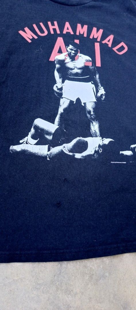 Muhammad Ali Graphic T-Shirt Black (Category: Tshirts & Polo Shirts ) located in Manila. Submitted by sandobag (Listing ID 1465815796, Image 3). Description: - Size: W 22.5 x L 30 - Issue nasa pic. - Color rate:10/10 - Color: Black - Design: Iconic Muhammad Ali graphic print with bold red text on the front, solid black back - Fit: Classic crew neck, standard fit - Condition: Good overall, with a couple of small pinholes near the bottom front hem 