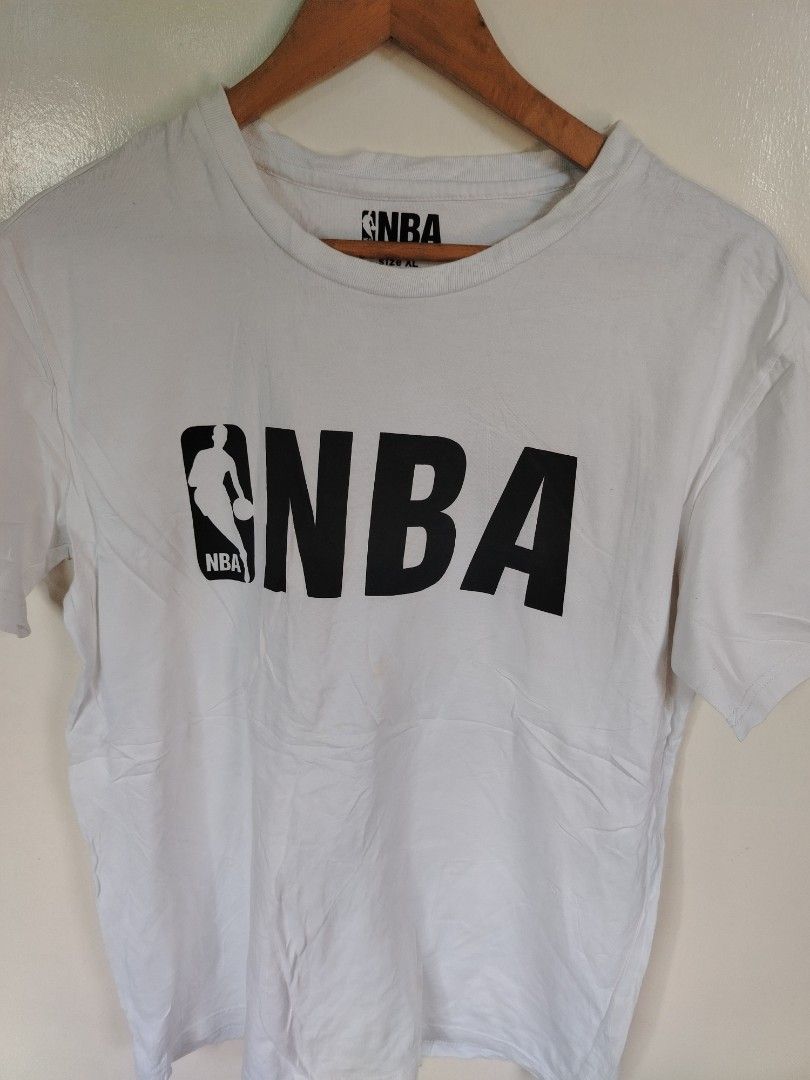 NBA White Logo T-shirt (Category: Tshirts & Polo Shirts ) located in Manila. Submitted by zyclothing03 (Listing ID 1465827943, Image 1). Description: - Color: Clean white with a solid black chest graphic - Size: XL (printed inside the collar) - Style: Classic crew neck, short sleeves, standard casual fit - Condition: Good, clean condition with mild wrinkles from storage - Perfect for everyday wear and basketball fans.