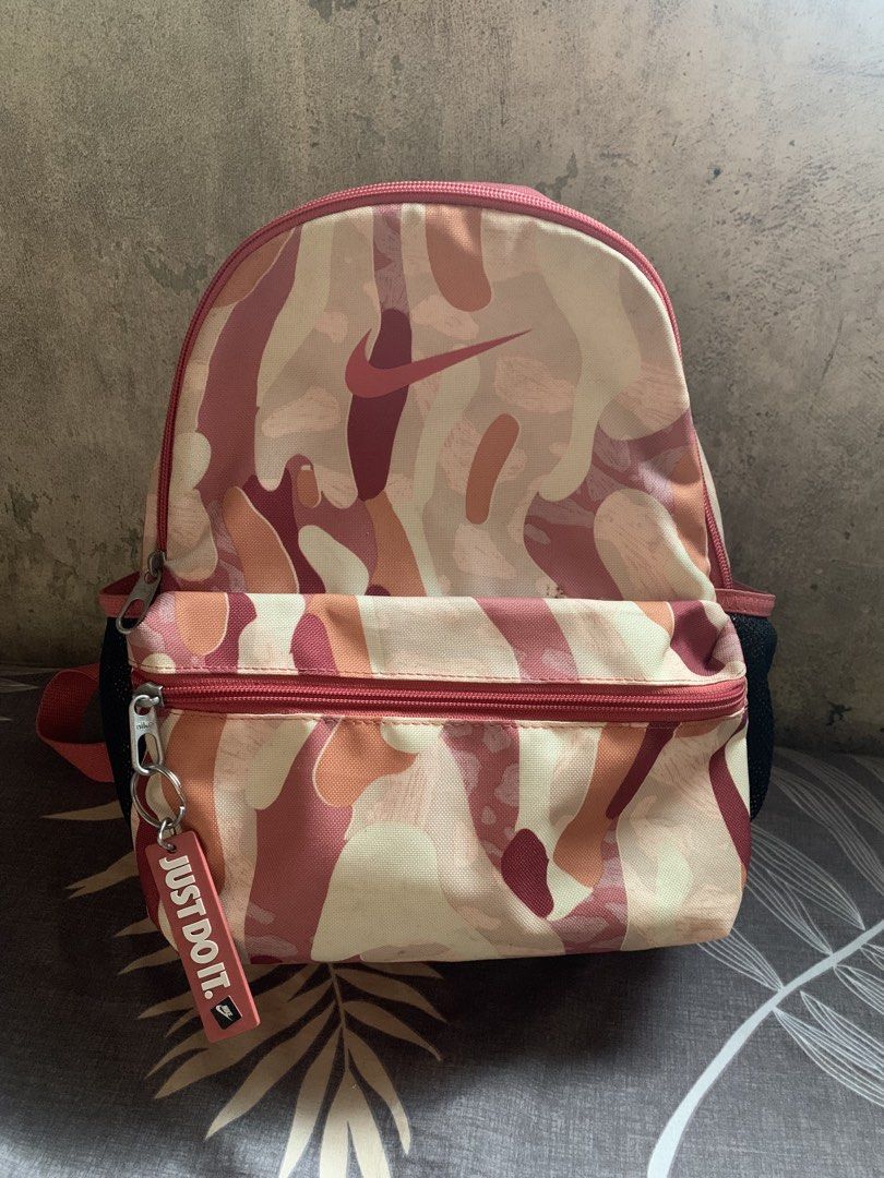 Nike Pink Camo Mini Backpack (Category: Backpacks) located in Valenzuela. Submitted by lovedeclutterph (Listing ID 1465788124, Image 1). Description: - Authentic Nike mini backpack in a stylish pink camo print - Front zipped pocket accented with a signature 'Just Do It' zipper pull tag - Spacious main compartment with convenient pink mesh side pockets for water bottles or umbrellas - Adjustable shoulder straps with padded backing for all-day comf