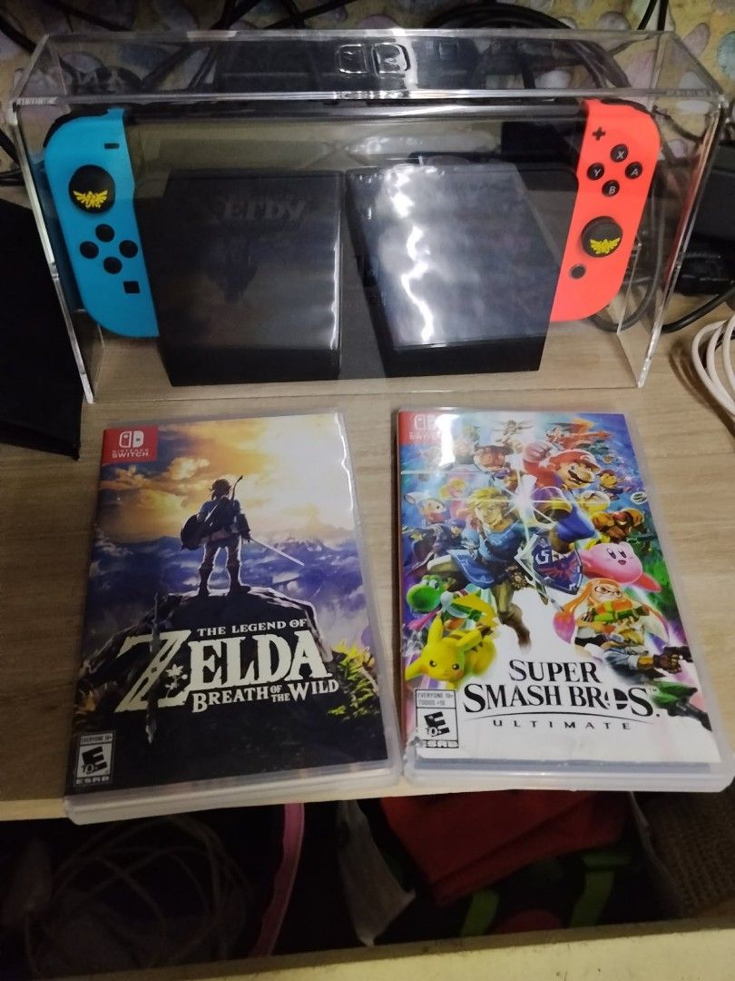 Nintendo Switch Console with Zelda and Smash Bros Games (Category: Nintendo) located in Pasay City. Submitted by 3j_shop (Listing ID 1465948166, Image 2). Description: - Nintendo Switch Console with Neon Blue & Neon Red Joy-Cons - Includes Zelda thumb grip caps installed on analog sticks - Physical Game 1: The Legend of Zelda: Breath of the Wild - Physical Game 2: Super Smash Bros Ultimate - Protected in a clear acrylic display case - Everything 