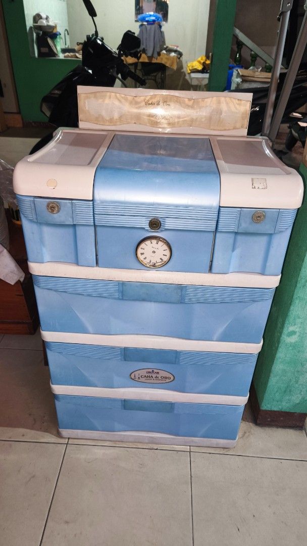 Orocan Caha de Oro Plastic Cabinet with Mirror (Category: Shelves, Cabinets & Racks) located in Bacoor. Submitted by fitatintin (Listing ID 1465935896, Image 2). Description: - Authentic Orocan Caha de Oro storage cabinet in stylish blue and white - 3 spacious bottom drawers for clothes and larger items - Convenient top compartment featuring a built-in mirror and smaller slots for makeup and accessories - Charming decorative clock design detail o
