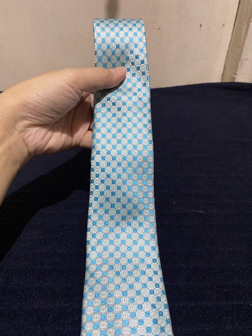 Paco Rabanne blue patterned silk necktie (Category: Ties) located in Manila. Submitted by resi.diaz (Listing ID 1465871977, Image 2). Description: - Material: 100% pure silk with silver woven background threads for a subtle shine - Design: Light blue with a checkered geometric pattern and small pink dot accents - Fit: Standard width, ideal for formal wear, business meetings, and office attire - Details: Authentic brand labels stitched on the back