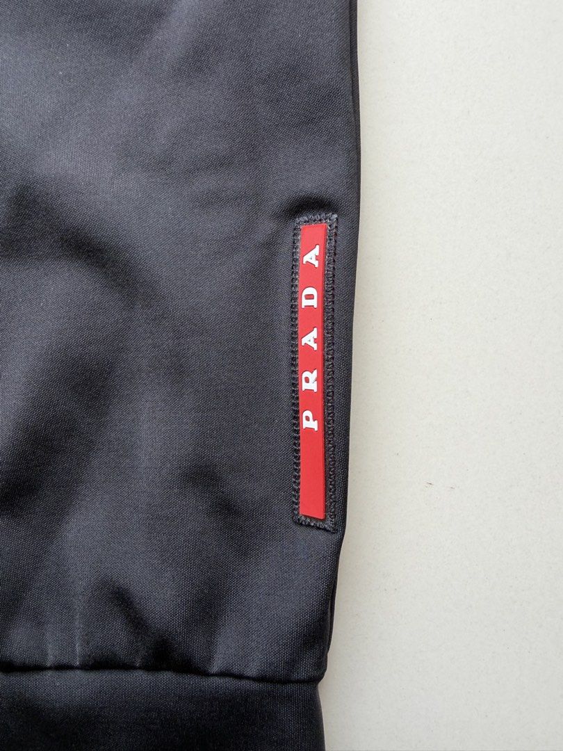 Prada Black Jogger Pants (Category: Joggers) located in Lipa City. Submitted by cokelight11 (Listing ID 1465799886, Image 2). Description: - Brand: Prada - Color: Black - Material: Premium technical fabric with comfortable stretch - Waistband: Elasticated with adjustable drawstring cords (32-36) - Pockets: Dual side pockets with waterproof zippers, Prada Milano branding, and riri hardware - Branding: Iconic red rubber Prada logo patch on the left
