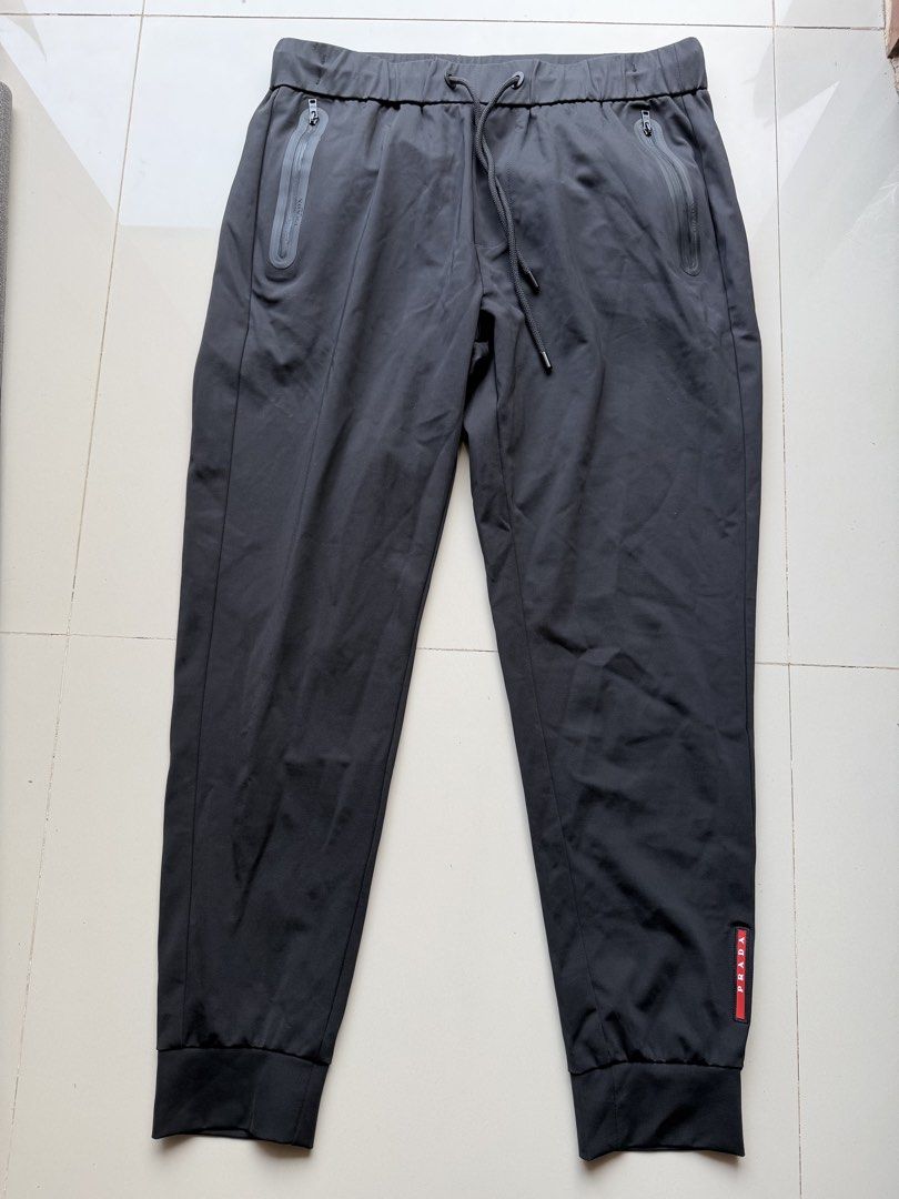 Prada Black Jogger Pants (Category: Joggers) located in Lipa City. Submitted by cokelight11 (Listing ID 1465799886, Image 1). Description: - Brand: Prada - Color: Black - Material: Premium technical fabric with comfortable stretch - Waistband: Elasticated with adjustable drawstring cords (32-36) - Pockets: Dual side pockets with waterproof zippers, Prada Milano branding, and riri hardware - Branding: Iconic red rubber Prada logo patch on the left