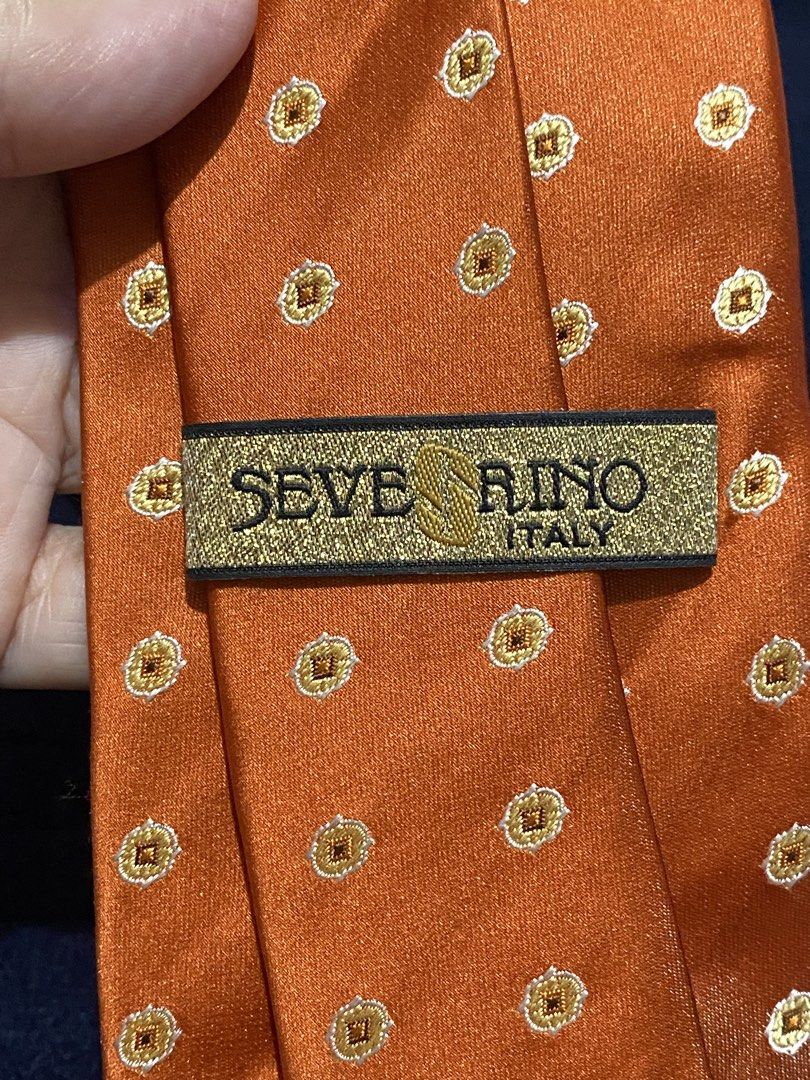 Severino Italy Silk Orange Necktie with Pattern (Category: Ties) located in Manila. Submitted by resi.diaz (Listing ID 1465836480, Image 3). Description: - Brand: Severino Italy - Material: 100% pure silk with a smooth texture and rich sheen - Design: Elegant orange base with a repeating gold and white geometric medallion pattern - Fit: Standard width silhouette, ideal for business attire and formal events - Condition: Brand new with original pri