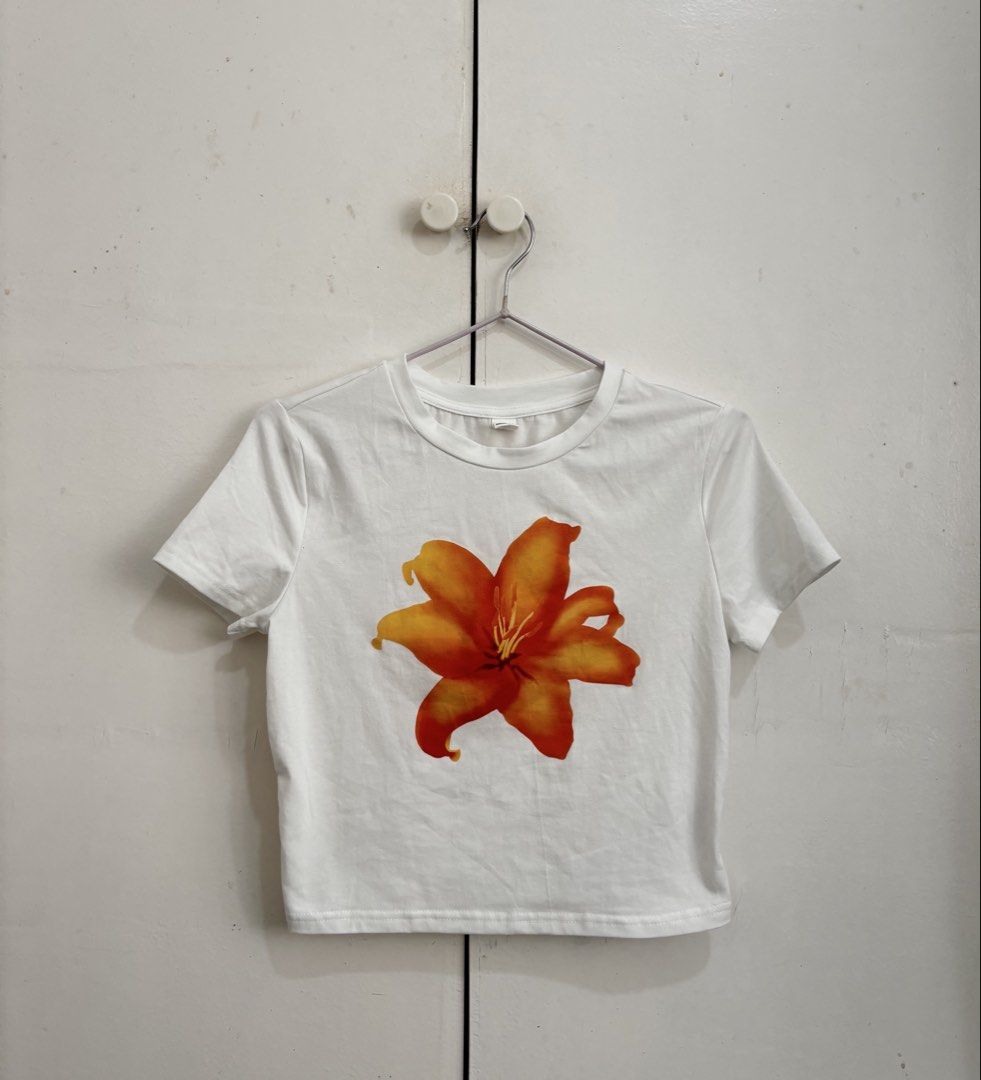 SHEIN White Crop Top Orange Flower (Category: Shirts) located in Manila. Submitted by dianafayesimbre (Listing ID 1465841556, Image 3). Description: - Brand: SHEIN - Size: Teen 15Y on tag but can fit xxs to semi medium frame womens - Design: Bold orange tiger lily graphic print - Details: Short sleeves, classic crew neck, stretchy fabric - Condition:Brand new - Styling: Perfect to pair with high-waisted shorts or jeans.